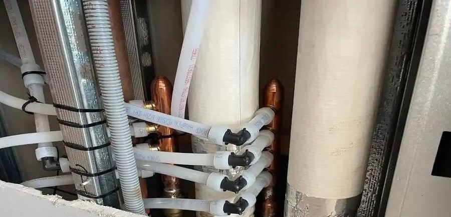 New PEX lines and copper risers run beside insulated stacks behind a wall